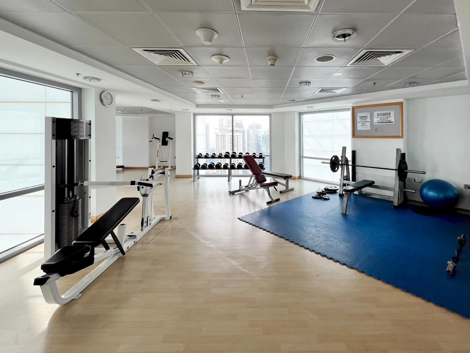 A bright gym with exercise machines, weights, and a blue workout mat.