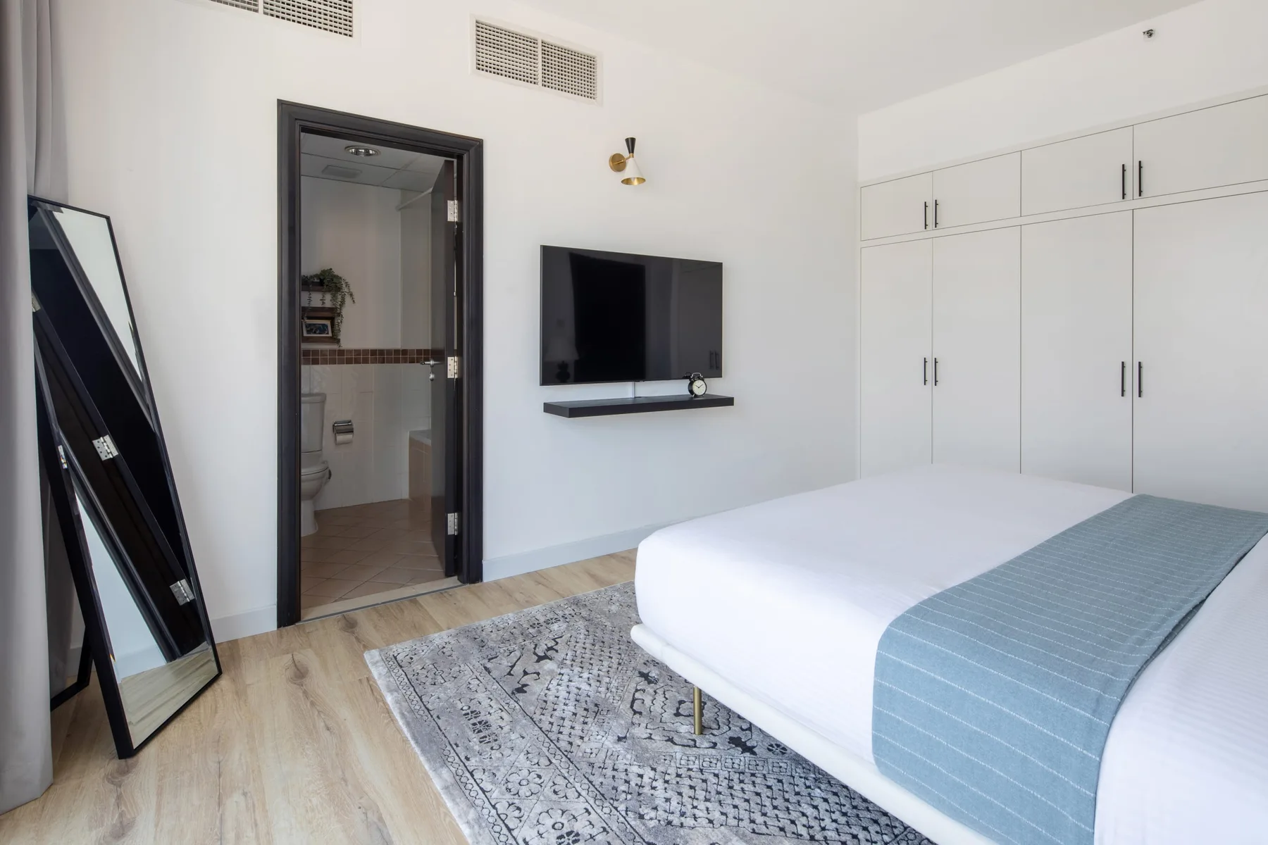A bright bedroom with a bed, wall-mounted television, and built-in wardrobes.