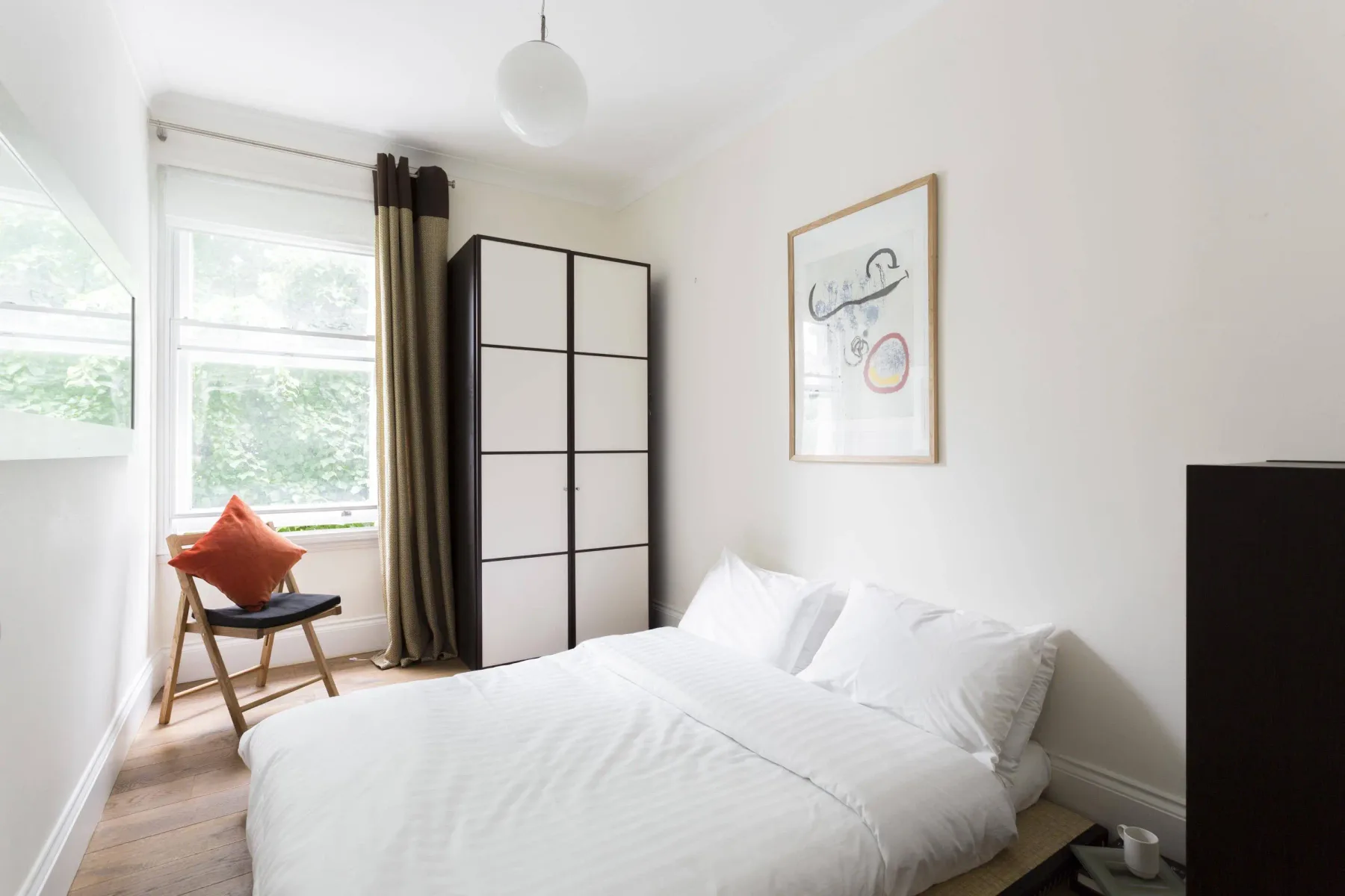 A bright bedroom with a white bed, a chair, and a large window.
