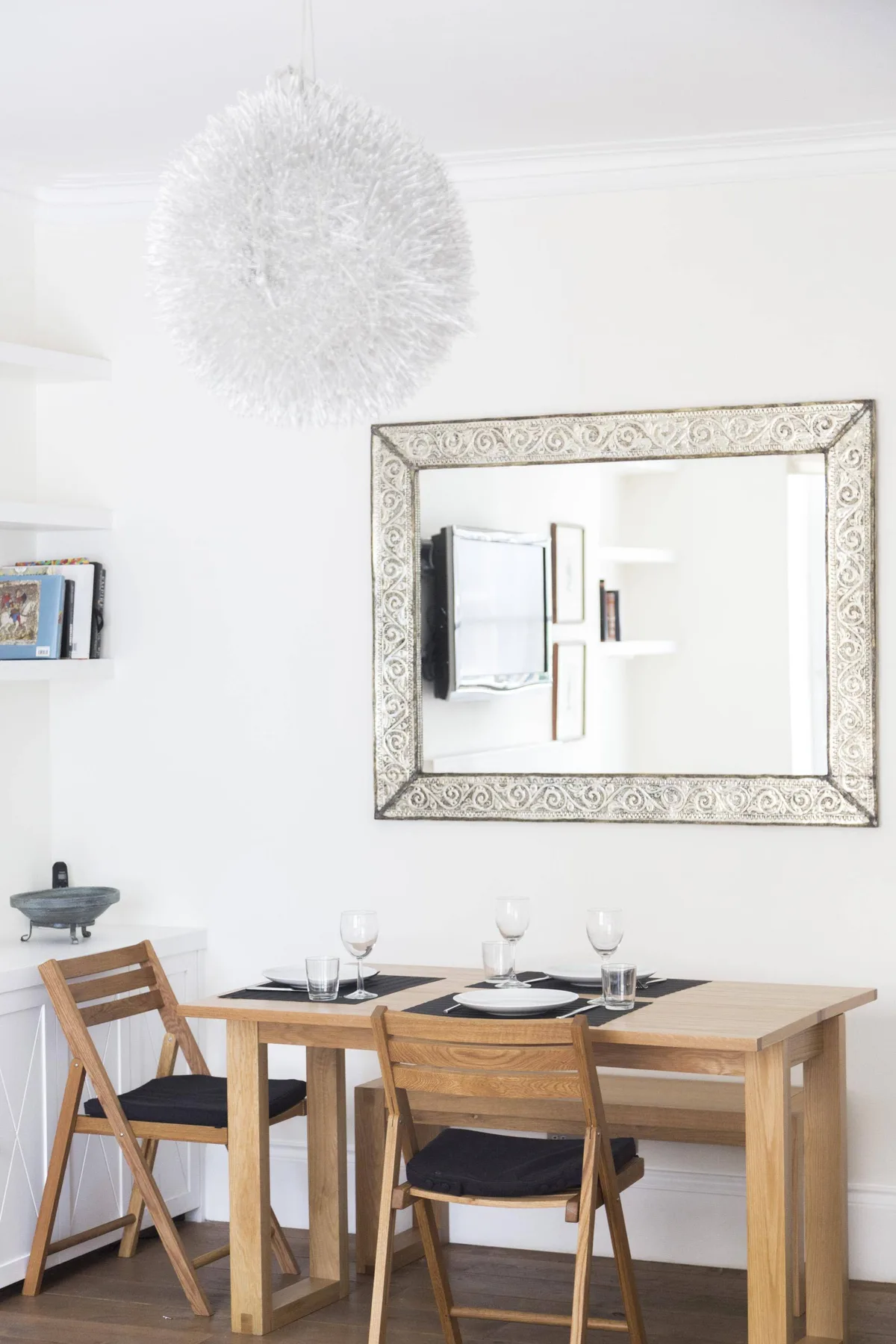 A dining area with a wooden table and chairs beneath a large framed mirror.