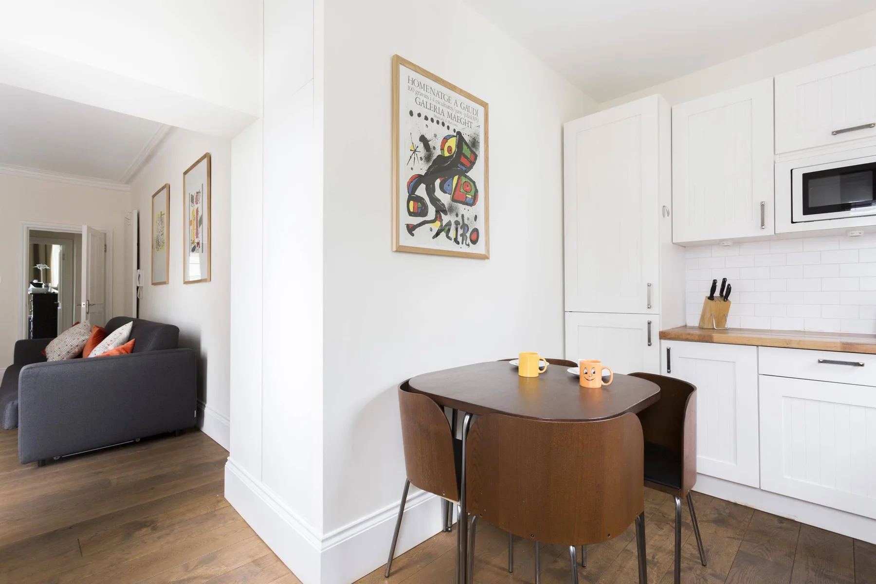 A bright dining area with a wooden table beside a white kitchen.