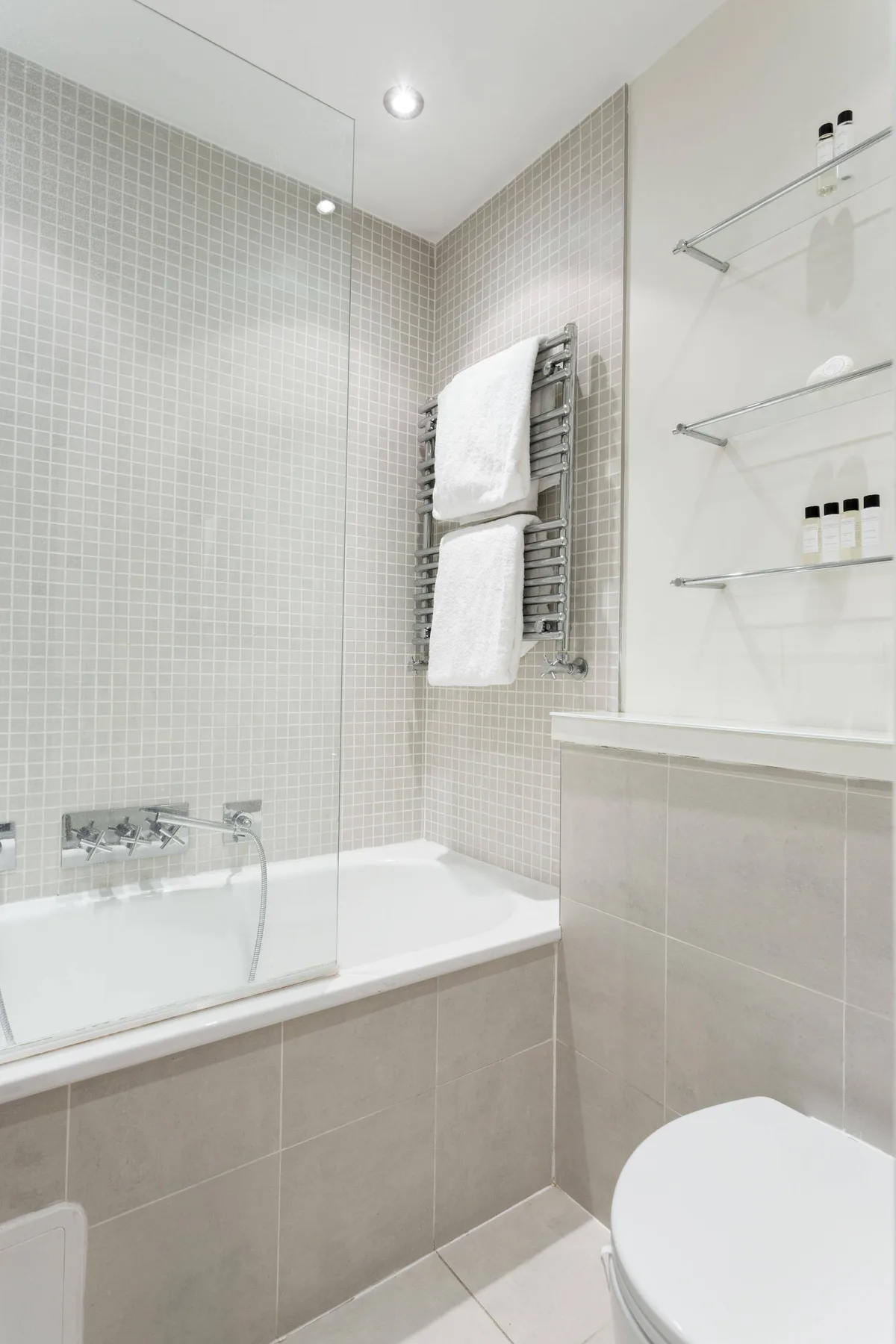 A tiled bathroom with a bathtub, wall-mounted towel warmer, and toilet.
