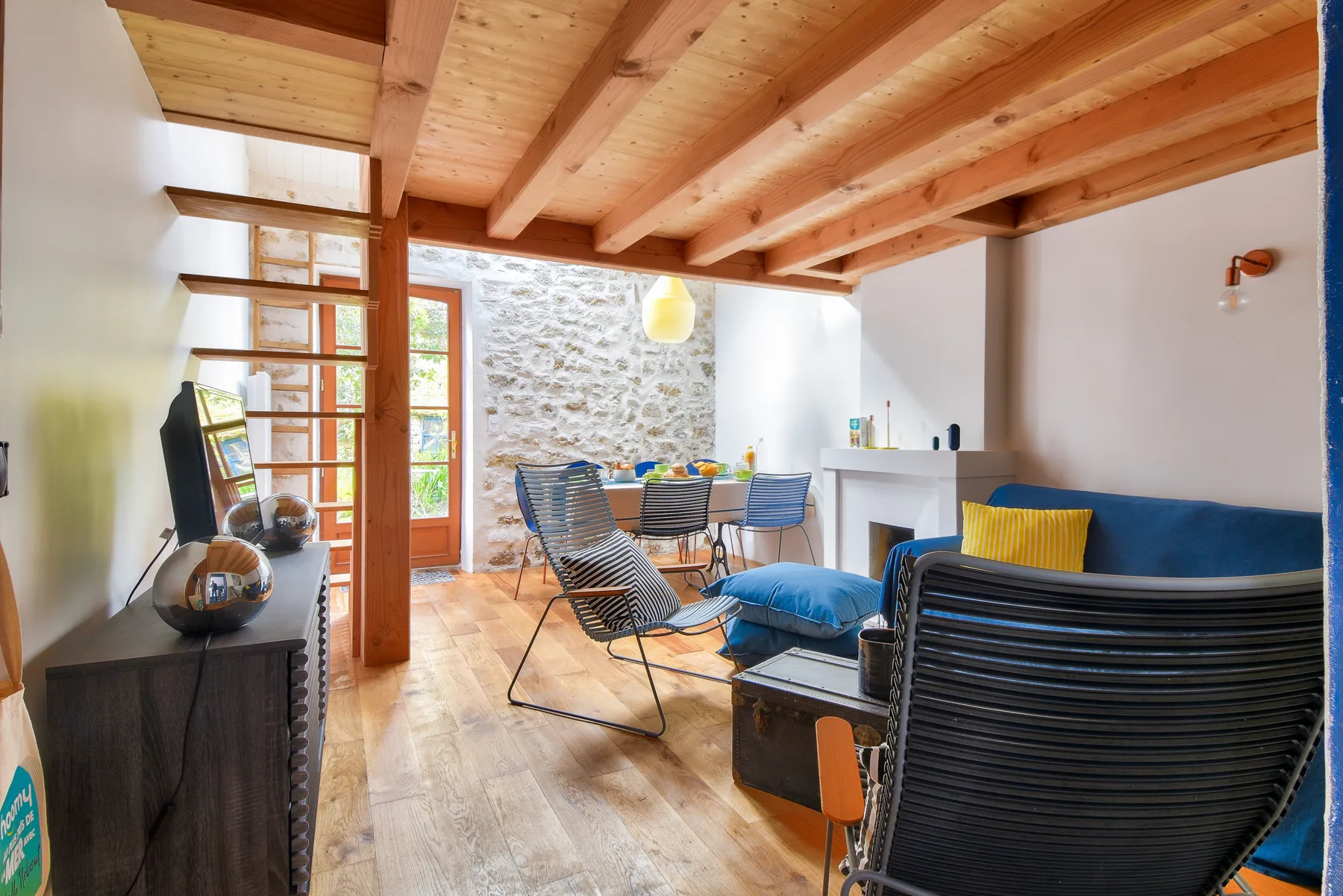 A bright living room with seating, a dining table, and exposed wooden beams.