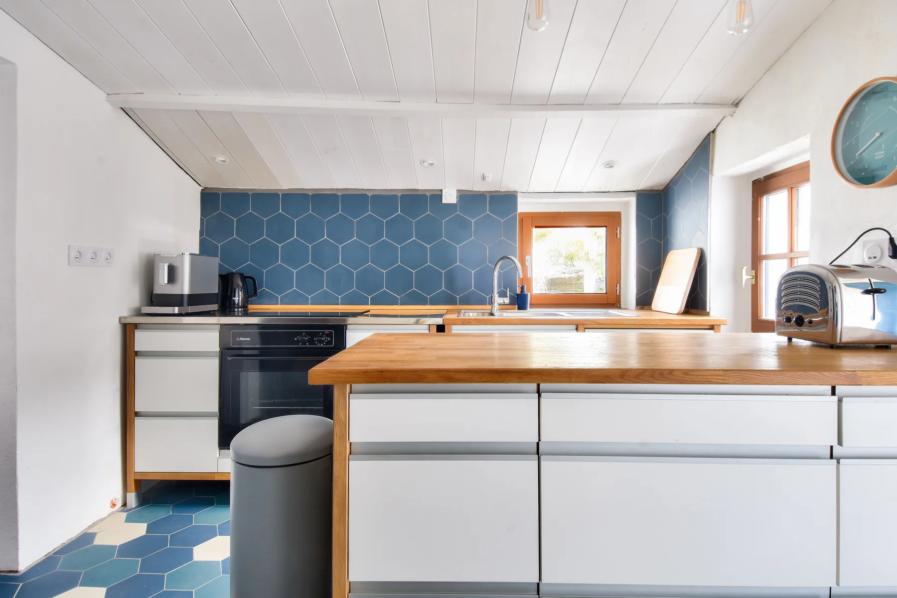 A bright kitchen with white cabinets, a wooden countertop, and blue tile.