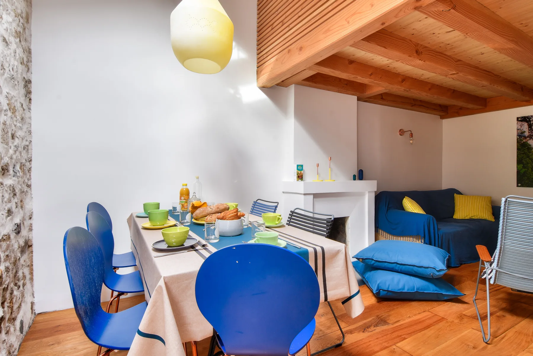 A dining area with a table and chairs beside a blue sofa and exposed wooden ceiling.