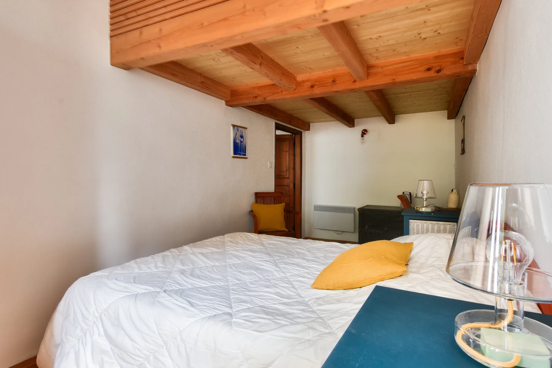A bedroom with a bed beneath an exposed wooden ceiling.
