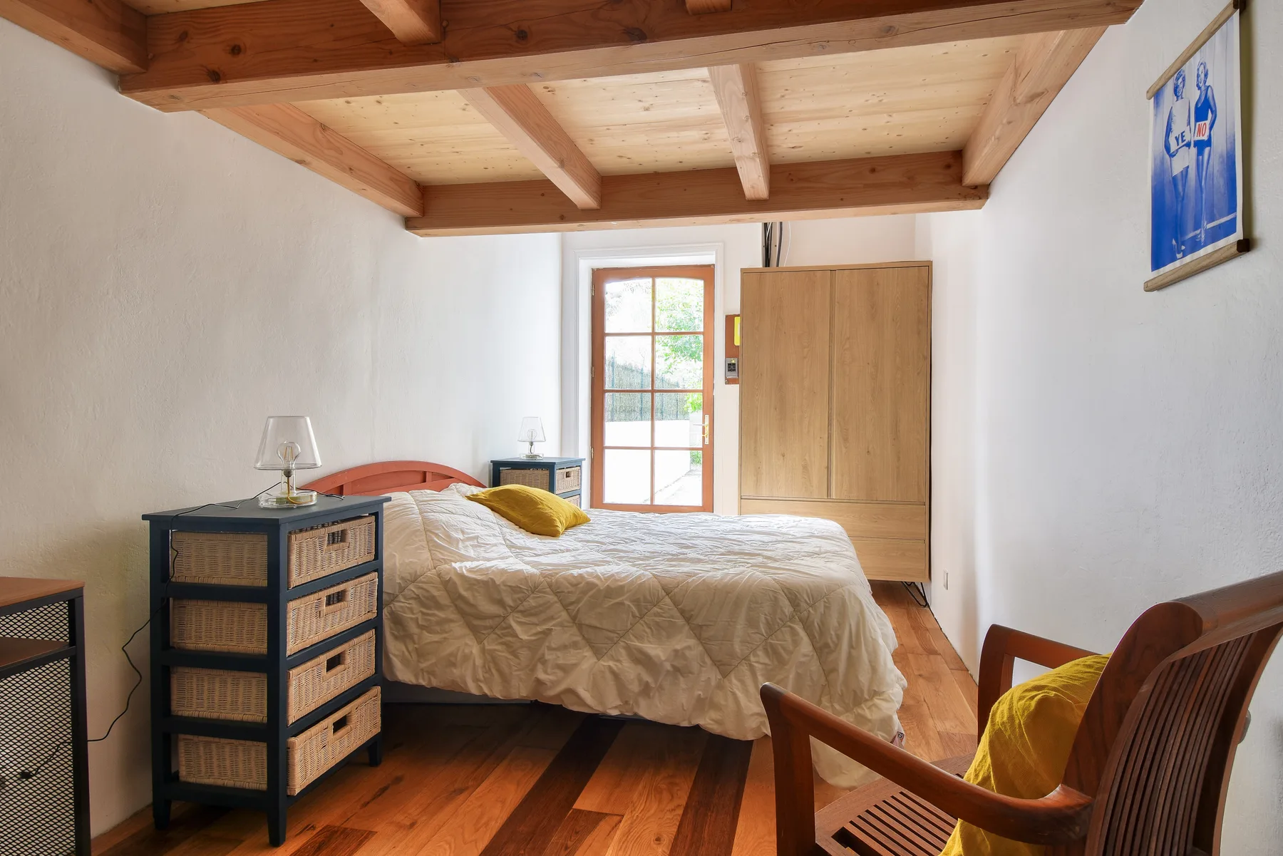 A bedroom with a bed, wooden ceiling beams, and a chair.