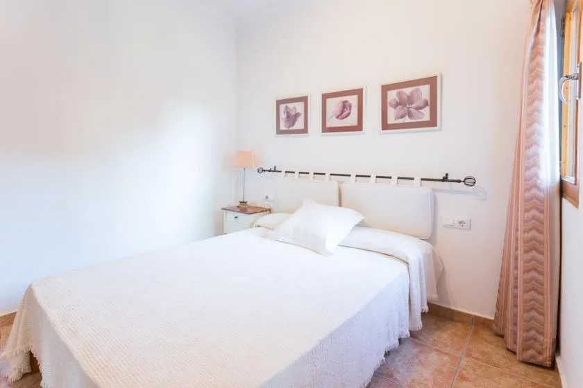 Un dormitorio luminoso con una cama, una mesita de noche y cuadros florales sobre el cabecero.