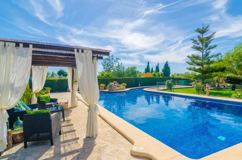 Una piscina junto a una zona de estar sombreada y un jardín.