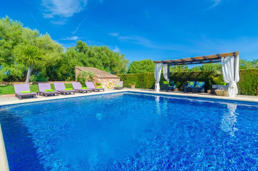 Una piscina al aire libre está rodeada de asientos y una pérgola con sombra.