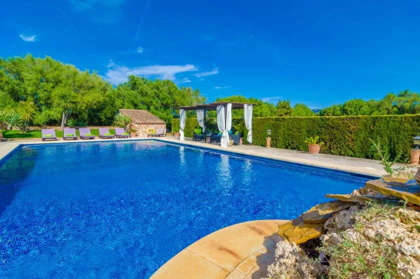 Una piscina al aire libre junto a una terraza pavimentada, tumbonas y una zona de sombra.