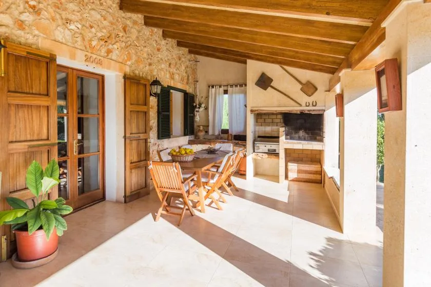 Un patio cubierto y luminoso con muebles de comedor de madera y una barbacoa empotrada.