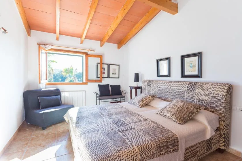 Un dormitorio con una cama grande, ropa de cama estampada y una ventana con vistas a la vegetación.