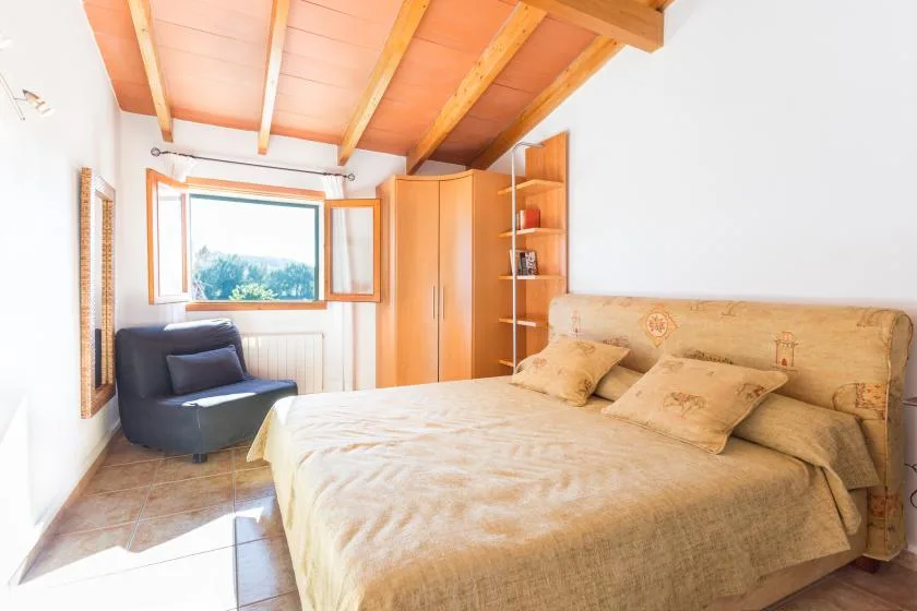 Un dormitorio con una cama grande, un sillón oscuro y una ventana.