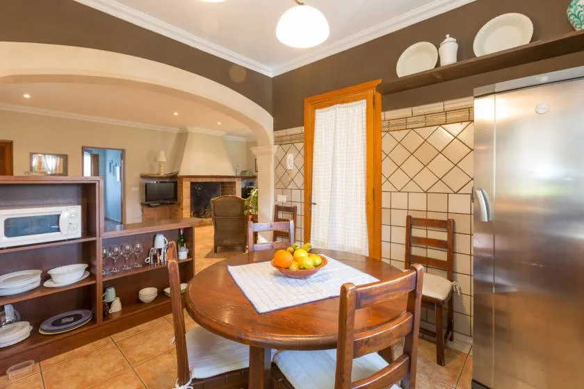 Comedor con una mesa redonda de madera junto a una pared de cocina revestida de azulejos.
