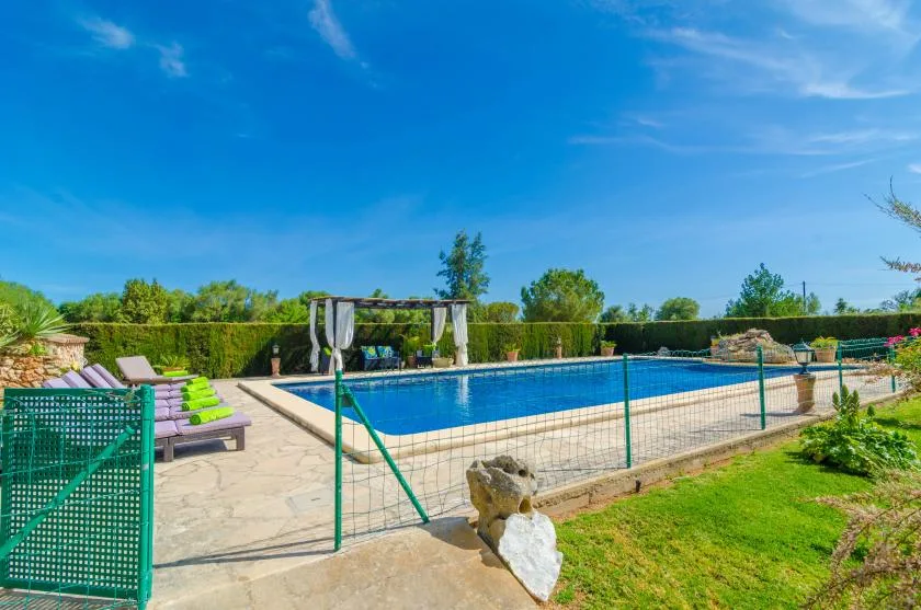 Una piscina al aire libre está junto a un patio pavimentado y un césped verde.