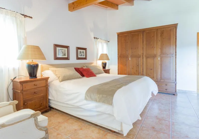 Un dormitorio luminoso con una cama grande, un armario de madera y mesitas de noche.