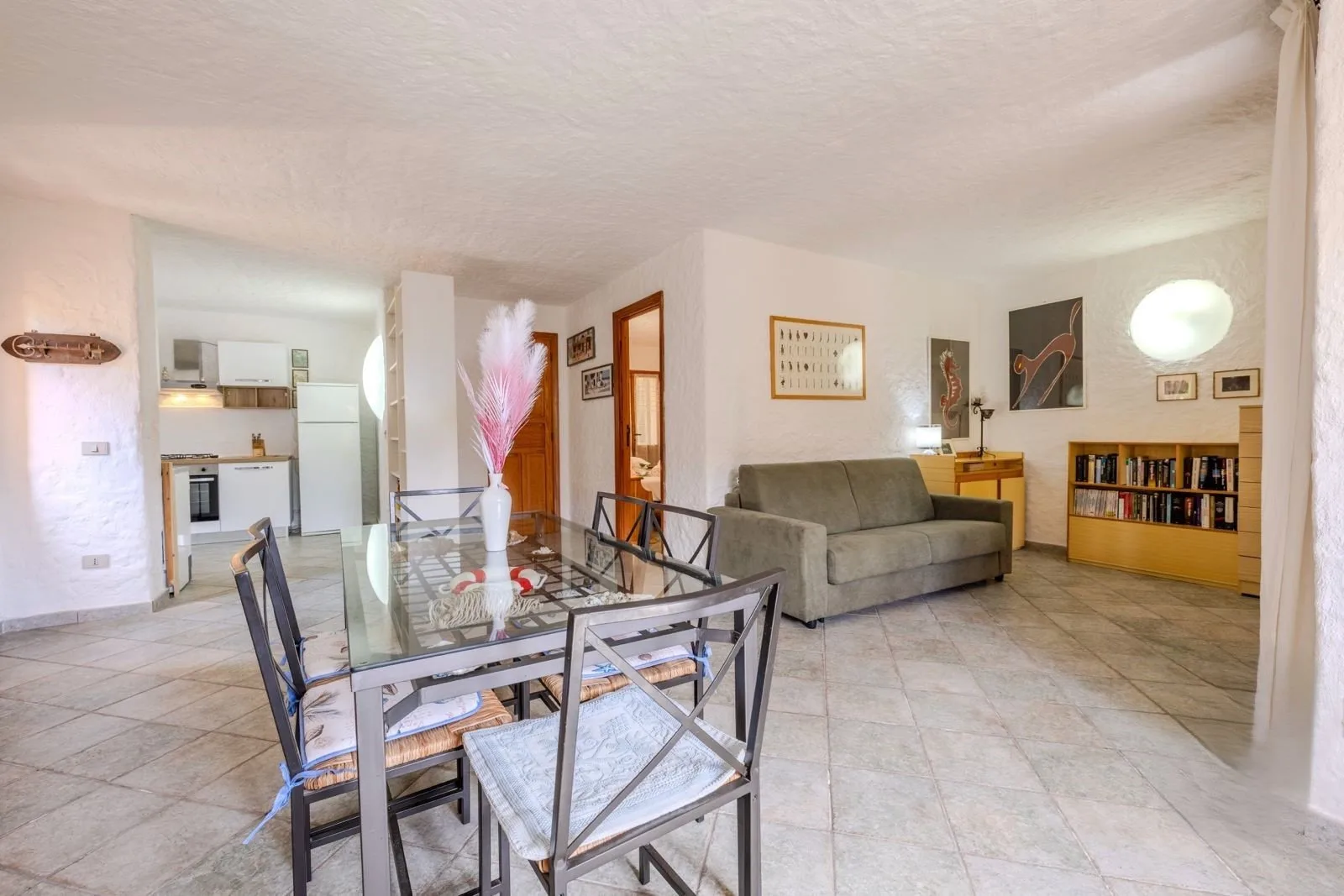 Sala de estar y comedor con mesa de vidrio, asientos y cocina abierta.