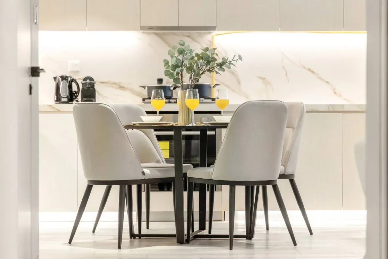Un comedor luminoso con asientos tapizados alrededor de una mesa y un jarrón con plantas.