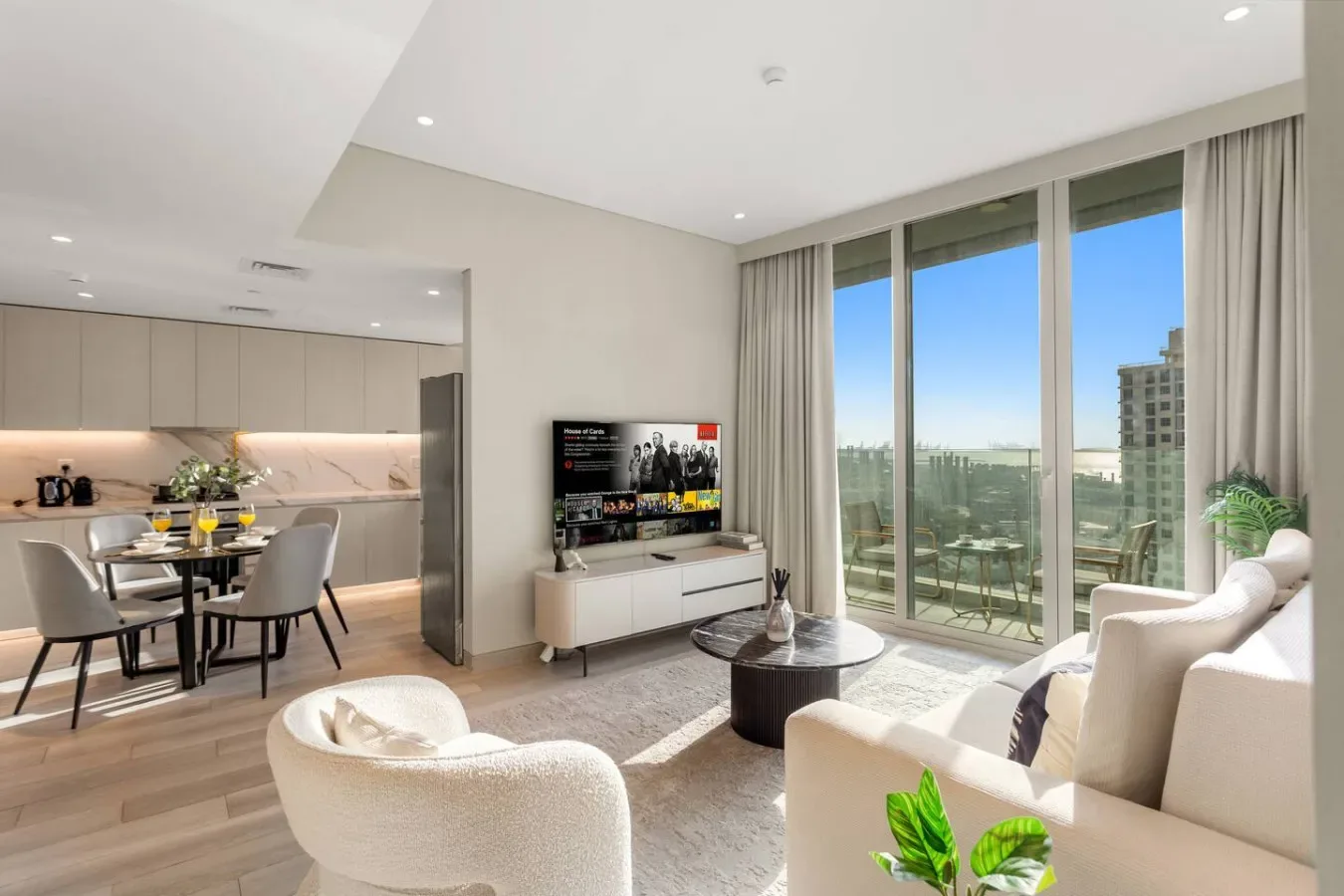 A bright living room with seating, a television, and large windows overlooking the city.