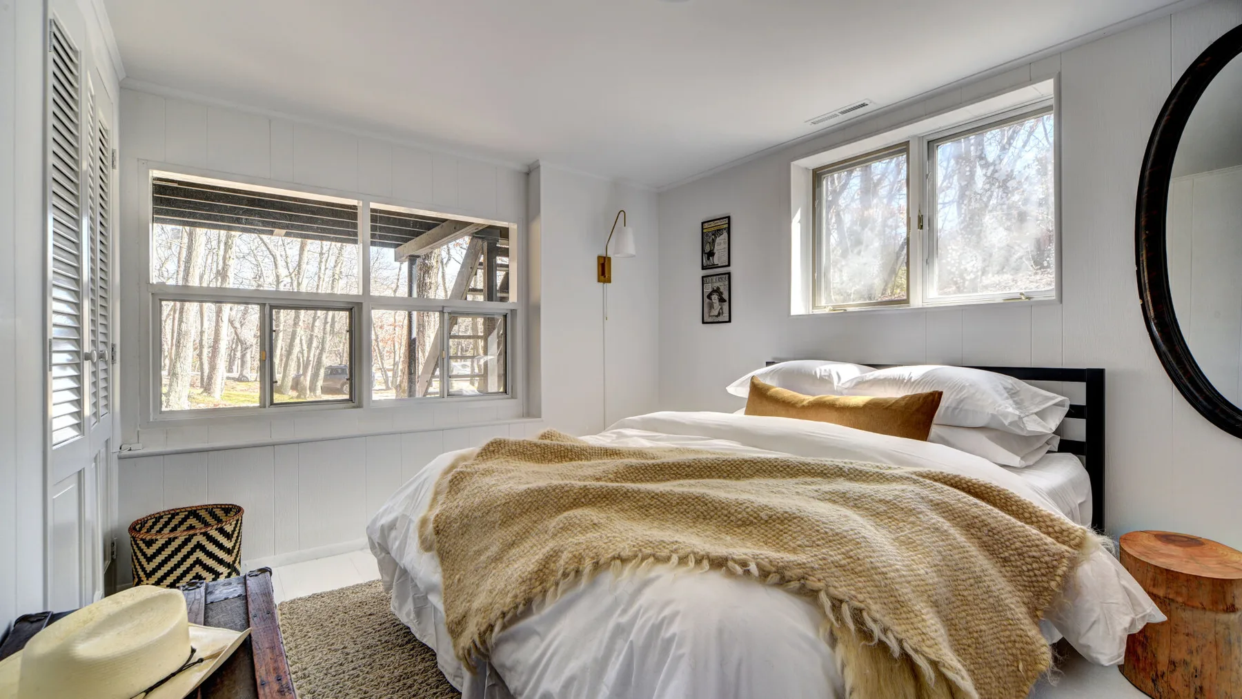 Un dormitorio luminoso con una cama bajo grandes ventanas y una manta texturizada.