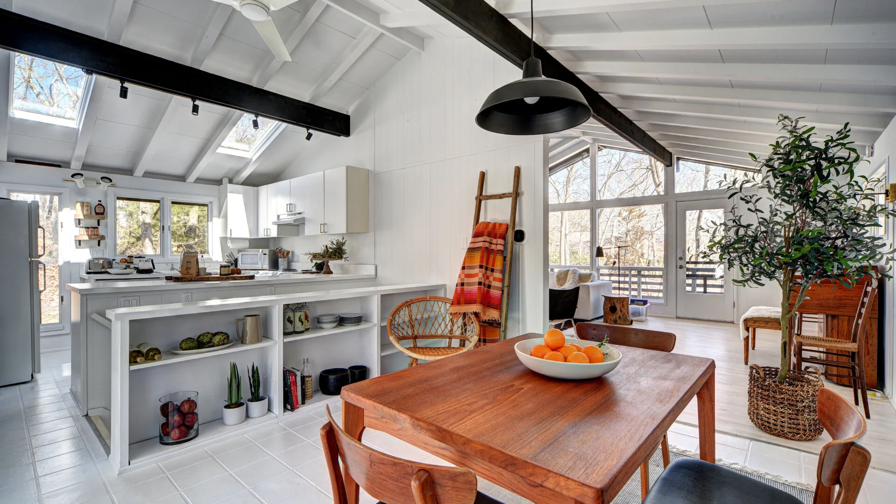 Una luminosa cocina abierta con comedor, mesa de madera y grandes ventanas.