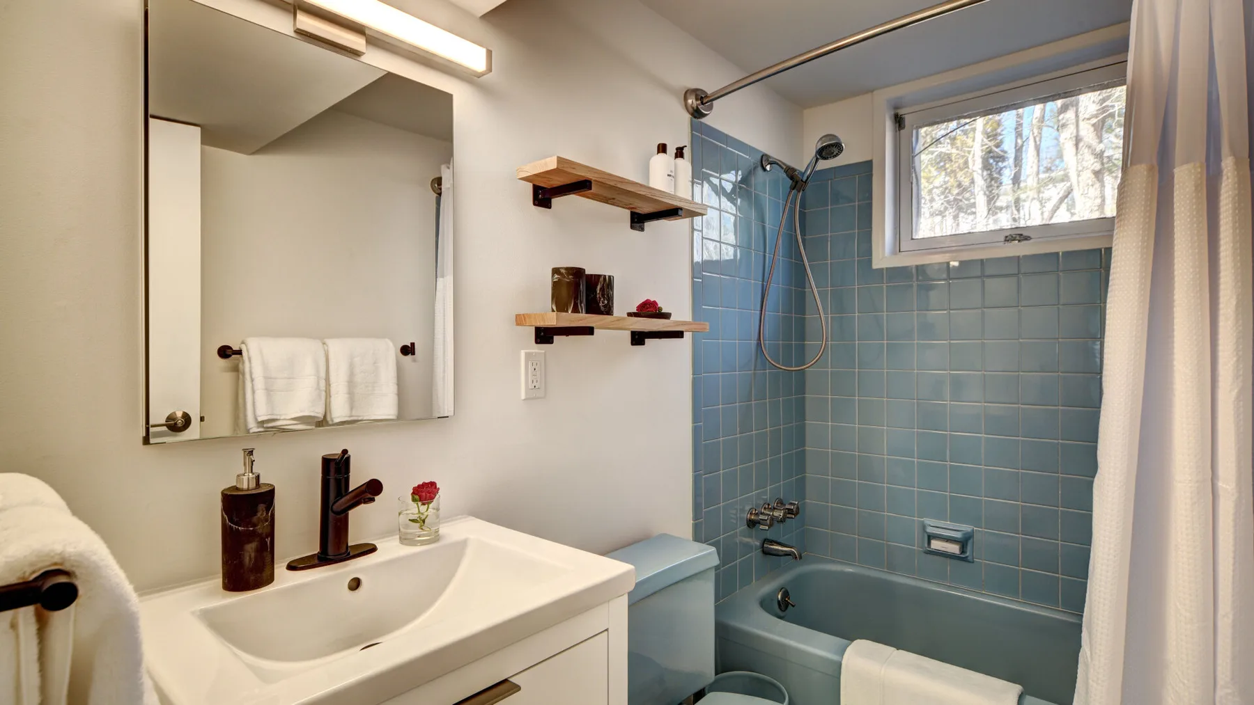 Un baño con lavabo, espejo y bañera con ducha revestida de azulejos.
