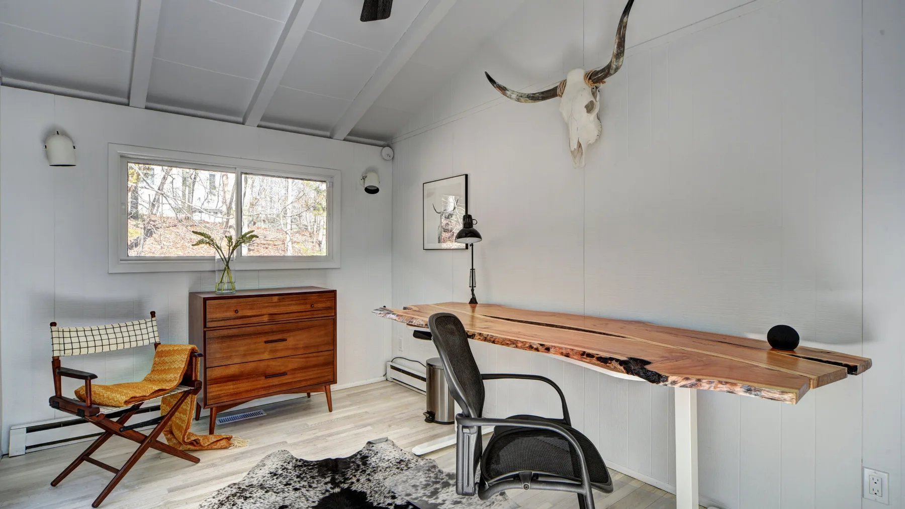 Un espacio de trabajo luminoso con un escritorio largo de madera, una silla y una ventana.