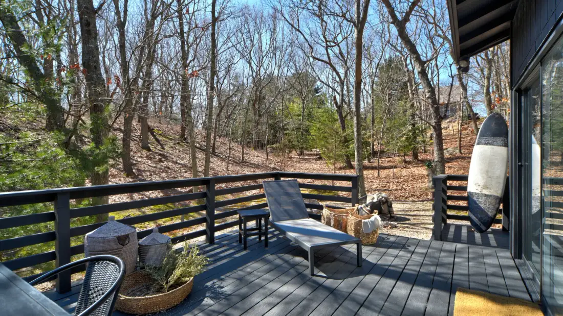 Una terraza de madera con una silla reclinable da a un paisaje boscoso.