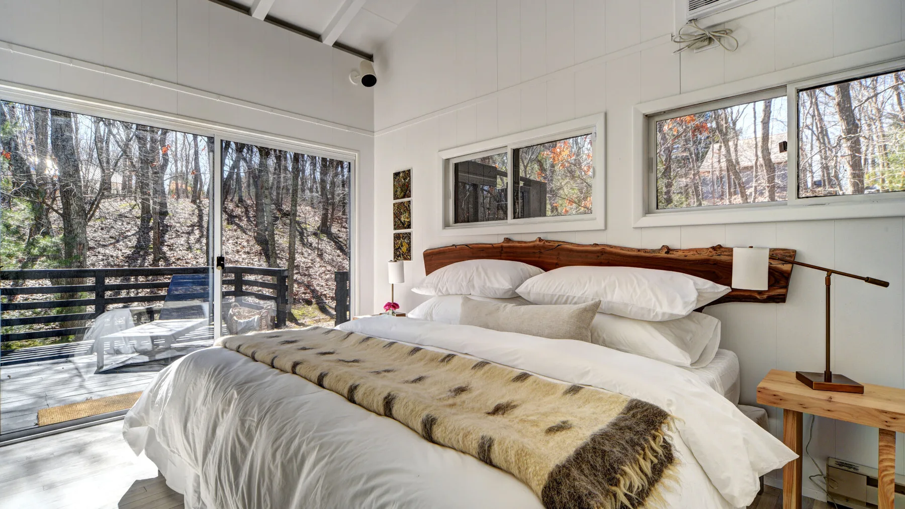 Un dormitorio luminoso con una cama grande y amplias ventanas con vistas a los árboles.