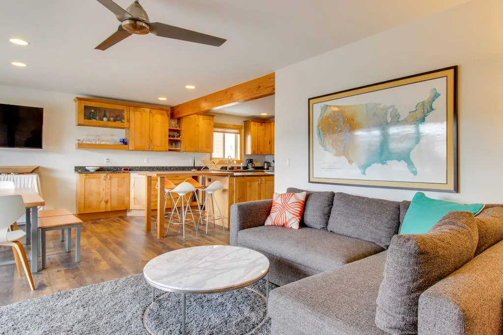 An open-plan living room and kitchen with a sectional seating area and a ceiling fan.
