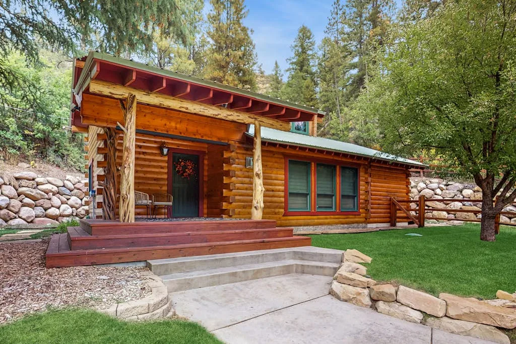 A log cabin exterior with a covered wooden porch and stone retaining walls.