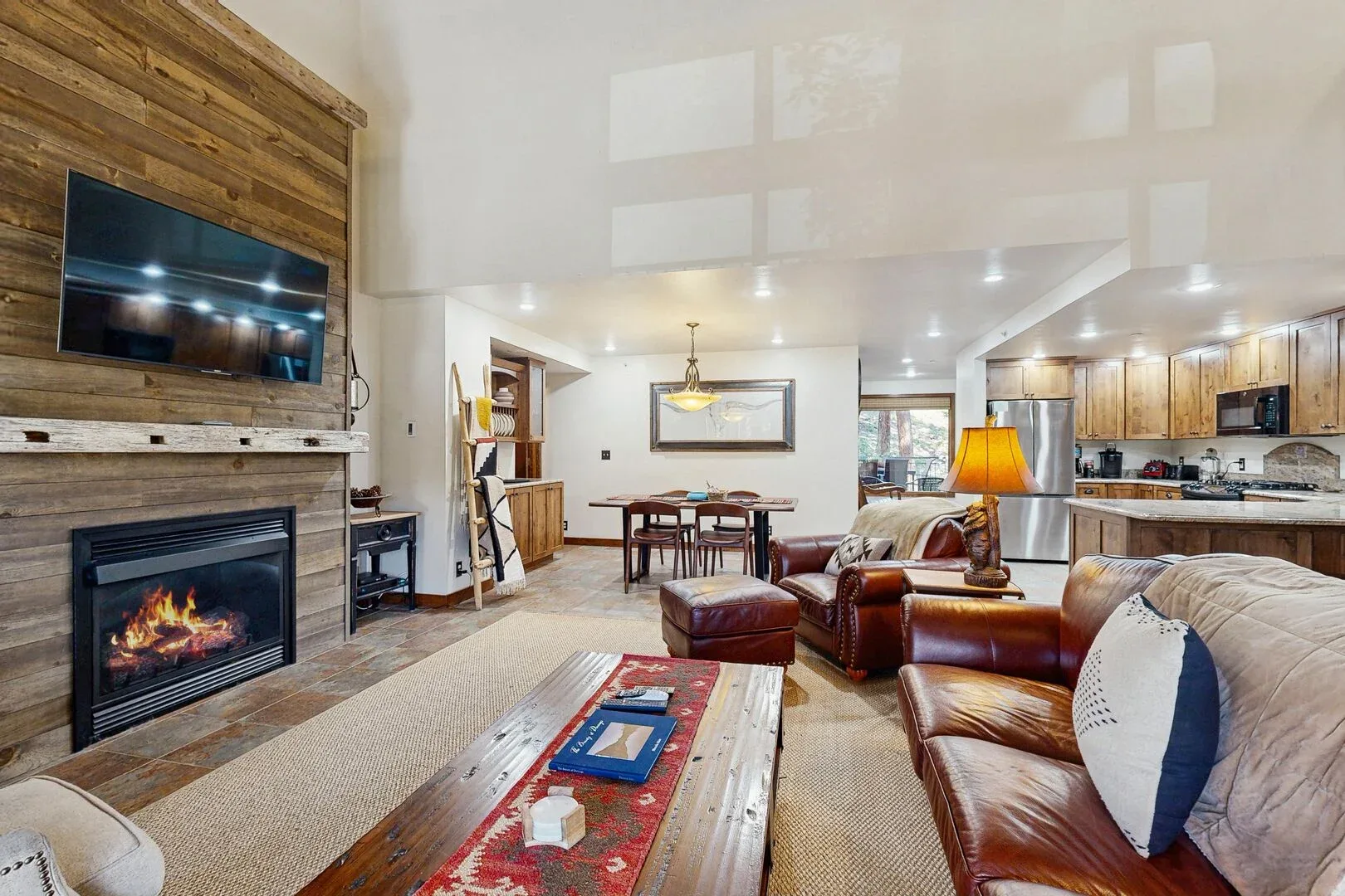 Open-plan living room with leather seating, a fireplace, and an adjoining kitchen.