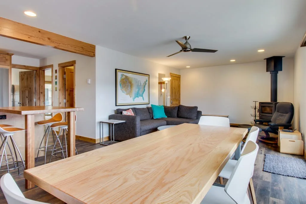 A dining area with a long wooden table and seating beside a living area.