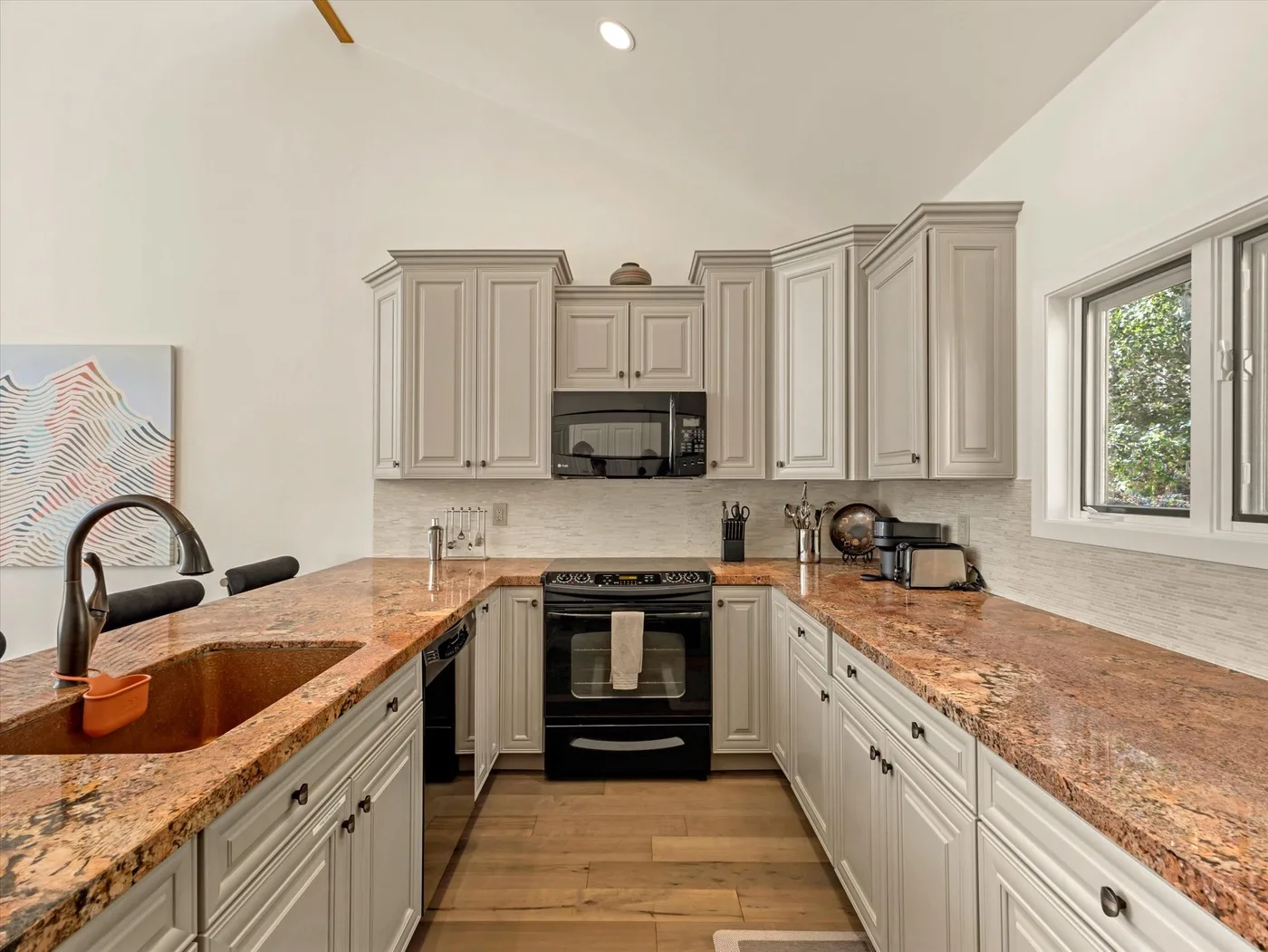 A bright kitchen with pale cabinetry, stone countertops, and a built-in oven.