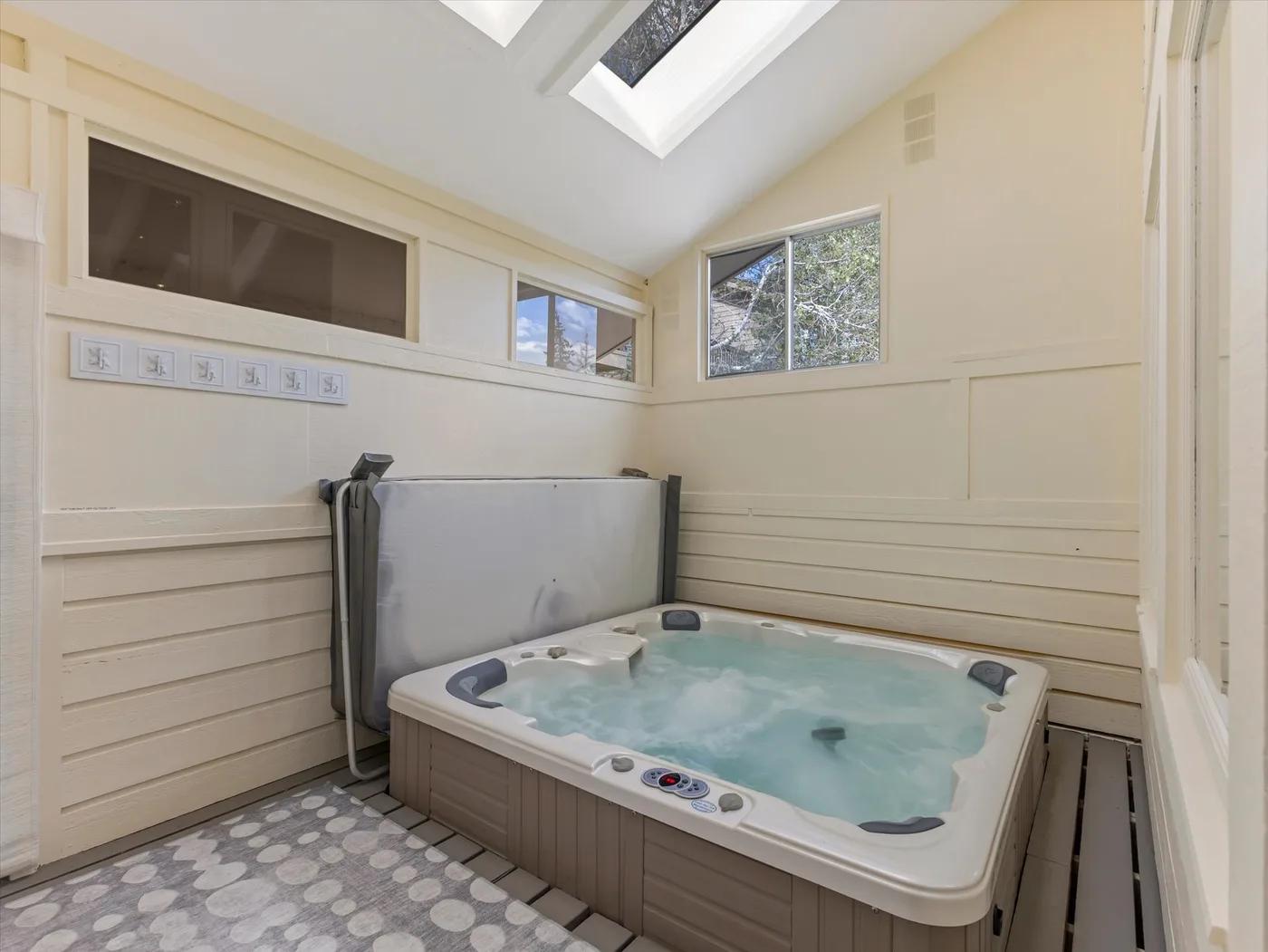 A bright indoor spa room features a large bubbling hot tub beneath skylights.