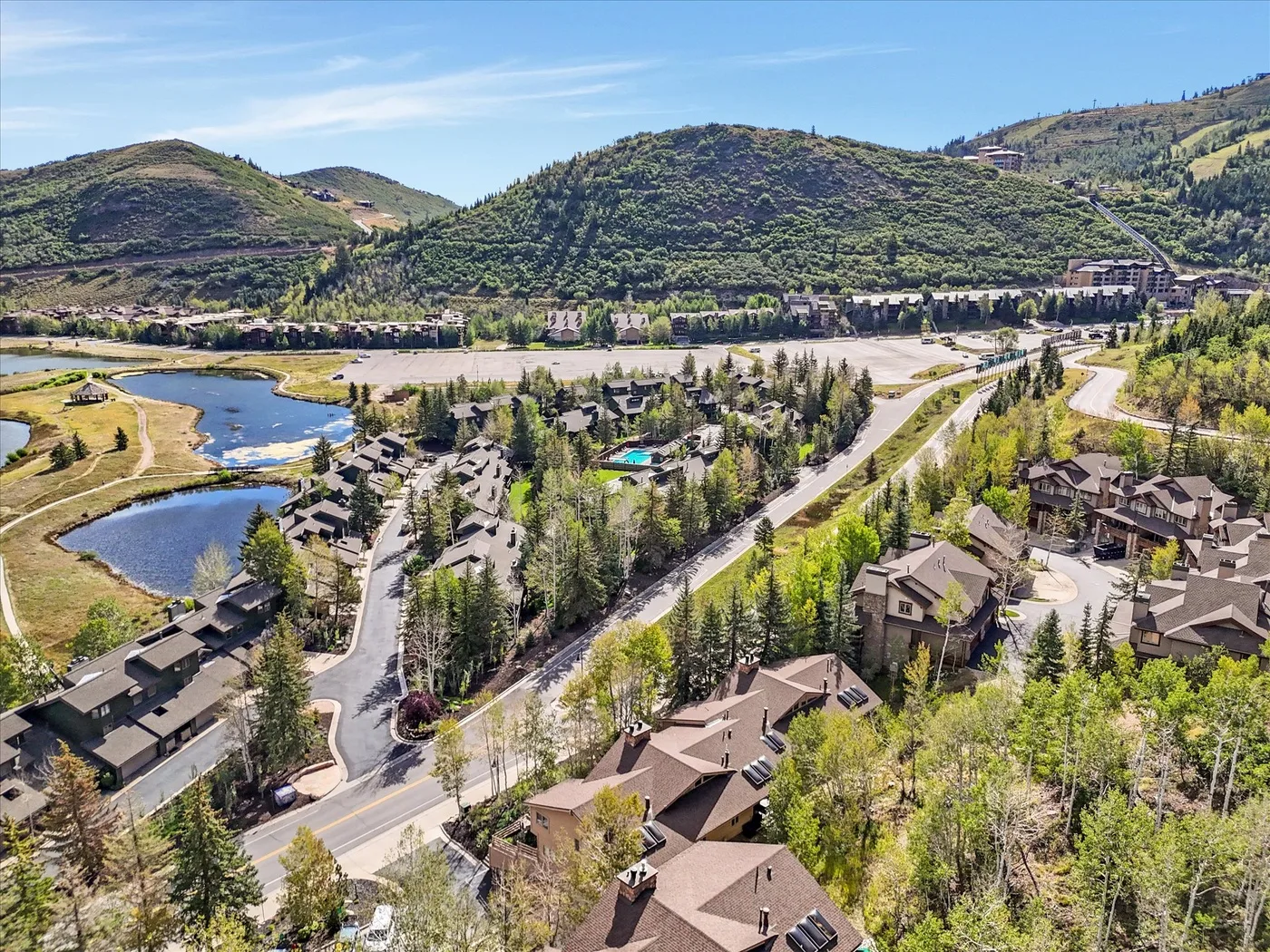 Aerial view of homes and roads among trees, with hills and a stream beyond.