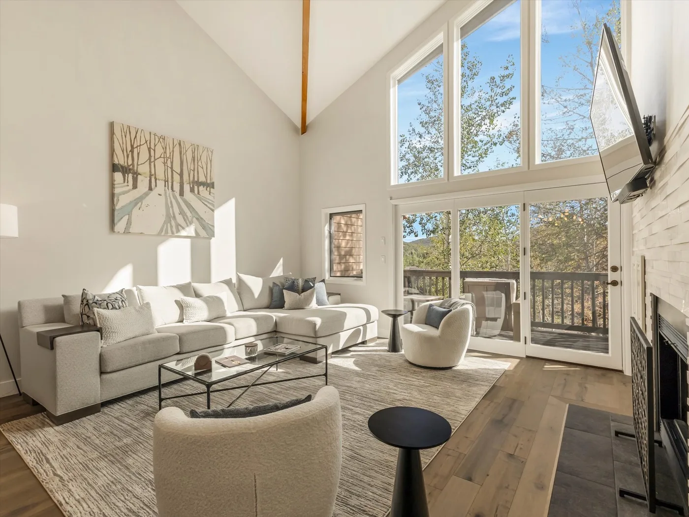 A bright living room with seating and large windows overlooking a wooded view.