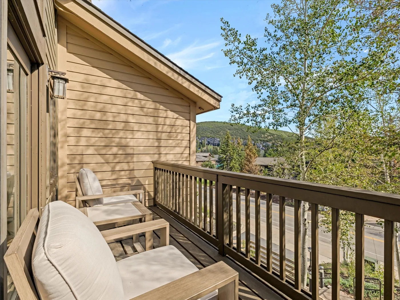 A wooden deck with cushioned seating overlooks trees and a distant hillside.