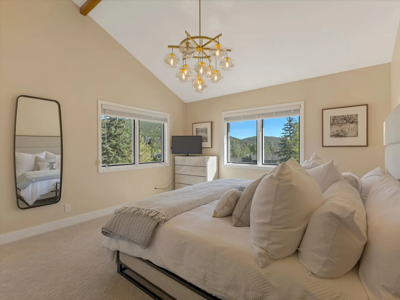 A bright bedroom with a large bed and windows overlooking trees.