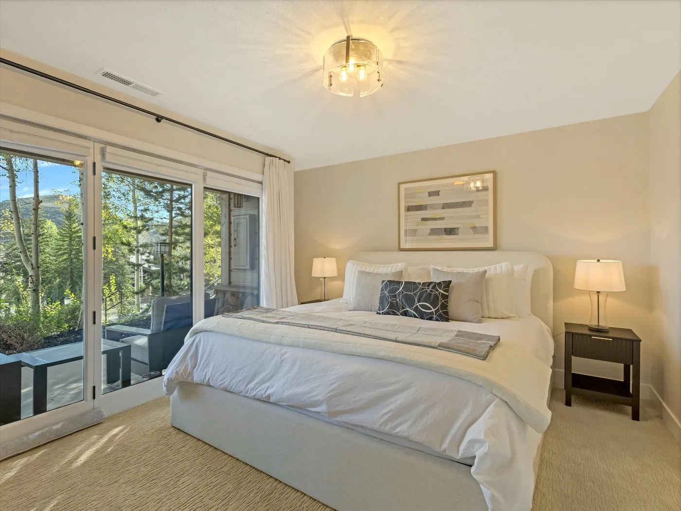 A bright bedroom with a neatly made bed beside large glass doors.