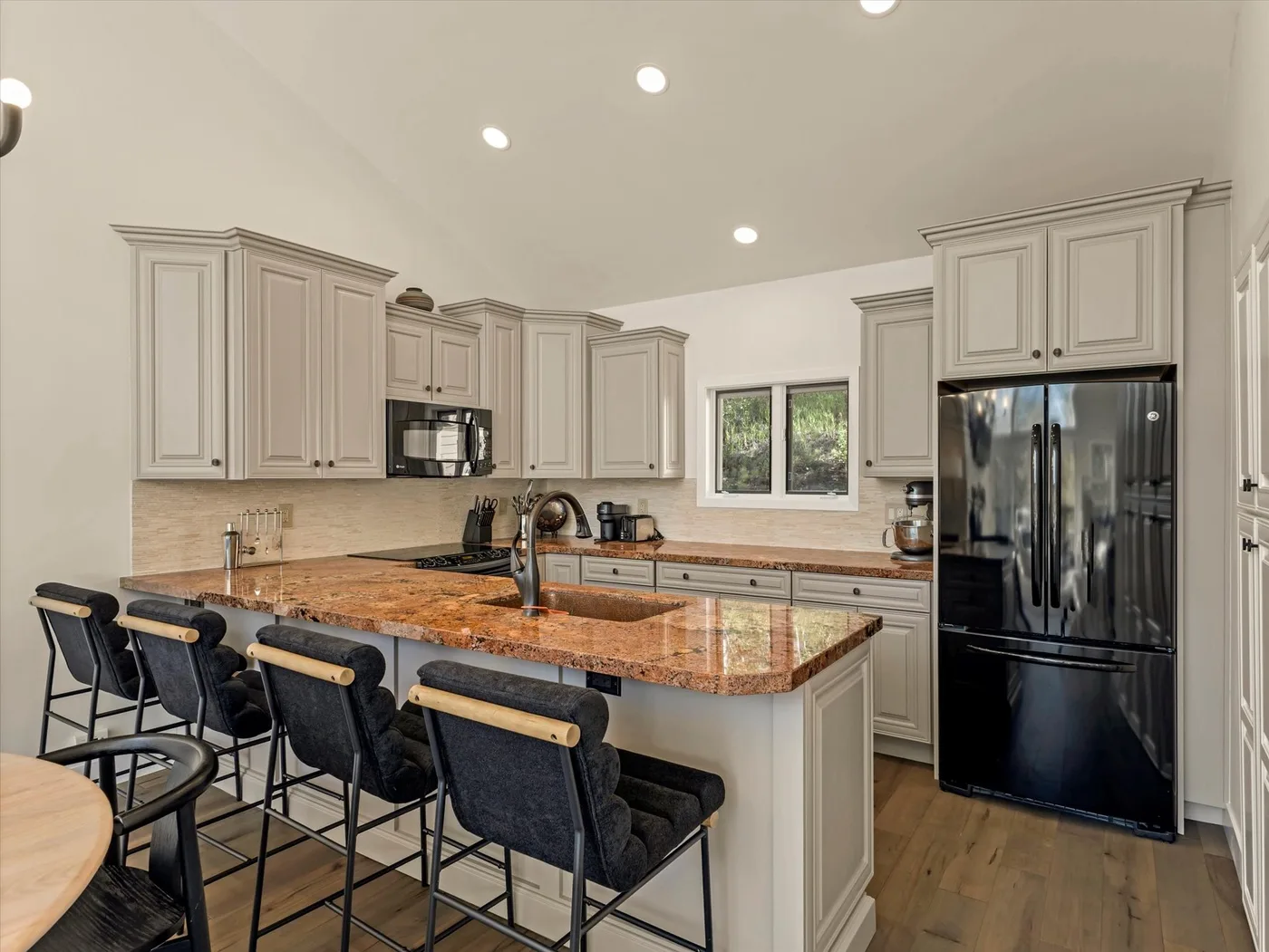 A bright kitchen with a large island, bar seating, and dark appliances.