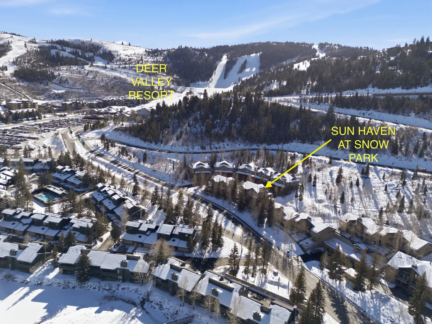 Aerial view of a snowy mountain resort with homes among evergreen trees.