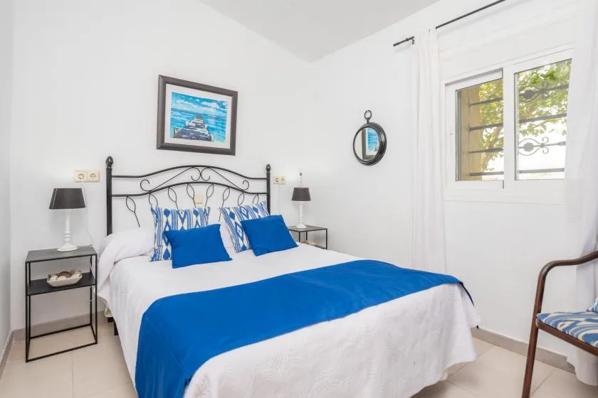 A bright bedroom with a double bed dressed in blue and white linens.