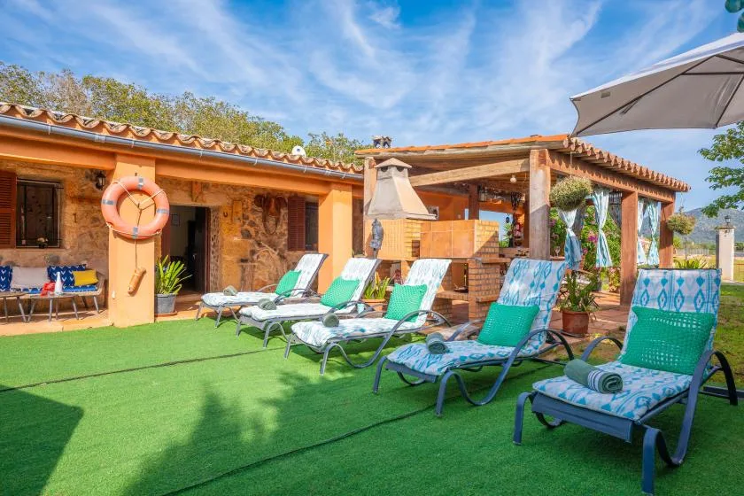 An outdoor patio with lounge seating, a shaded pergola, and a green lawn.