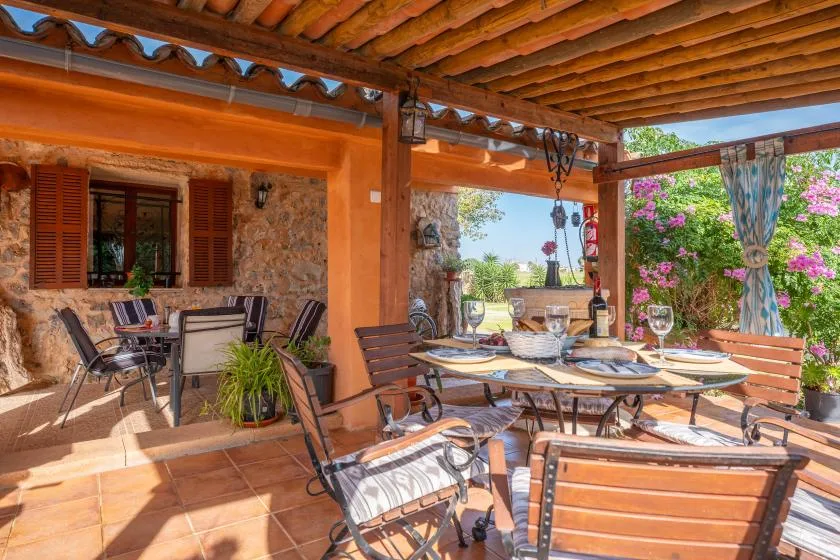 A covered outdoor dining area with a table and seating beside a stone wall.