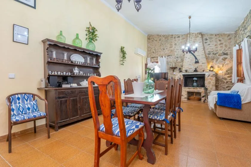 A dining room with a wooden table and chairs beside a stone fireplace.