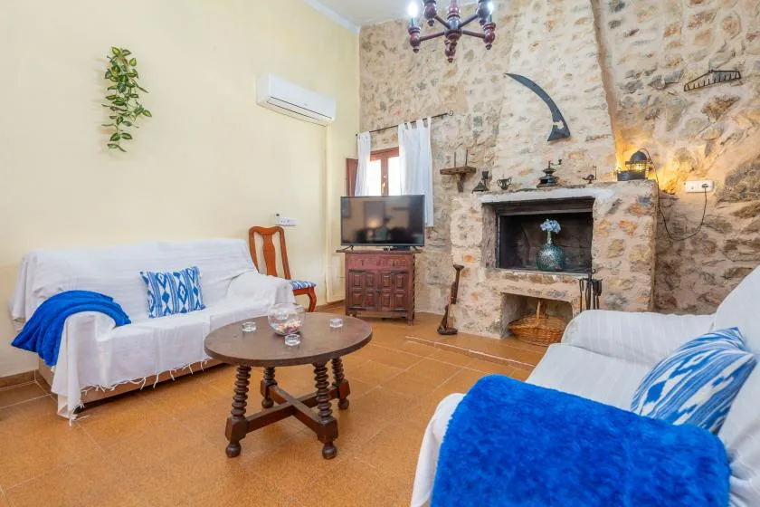 A rustic living room with seating, a television, and a stone fireplace.