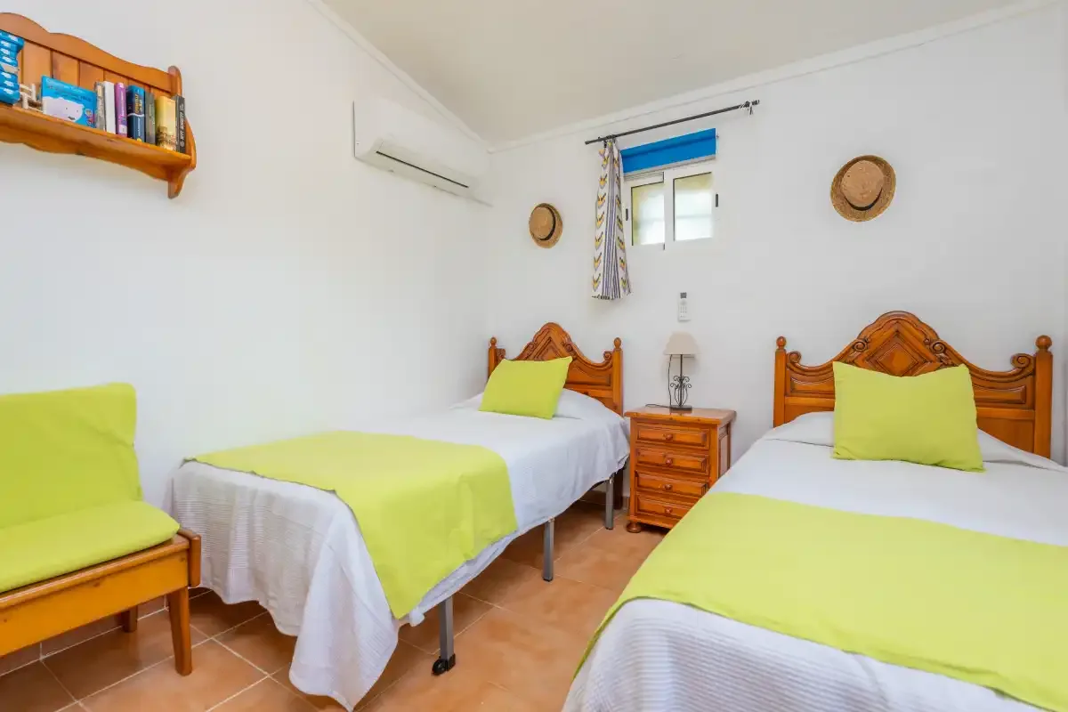 A bedroom with two beds, each dressed in white and bright green linens.