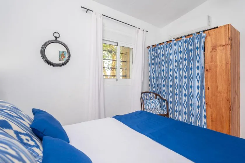 A bedroom with blue-and-white bedding, a patterned curtain, and a wooden wardrobe.